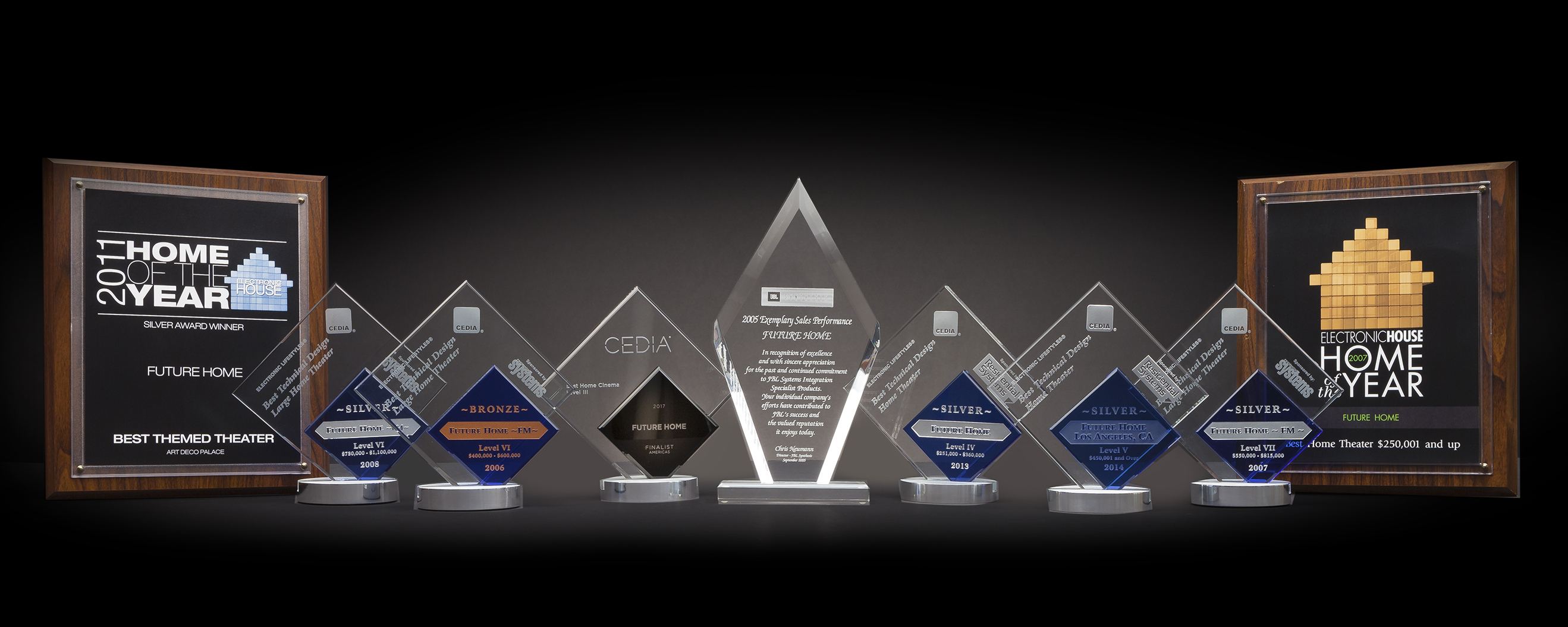 Line of eight crystal and wood trophies and plaques on a dark surface, highlighting Future Home’s multiple “Home of the Year” and CEDIA awards.