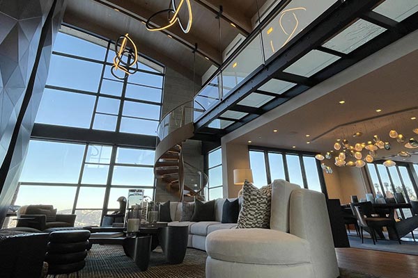 Bright loft-style living room with a tall, dark geometric-tiled fireplace, floating mezzanine, and modern furnishings around a round coffee table.