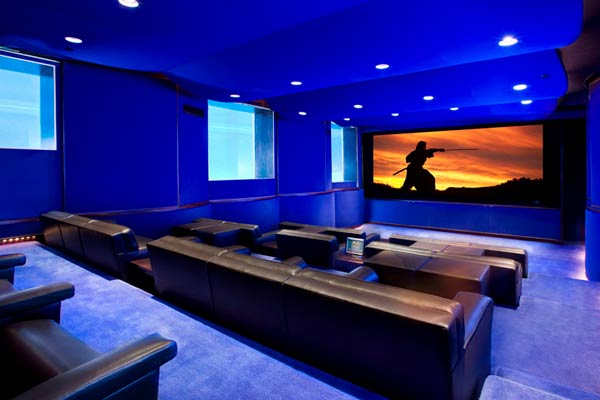 Modern home theater with minimalist design, featuring a wide screen, low-profile seating, dark acoustic wall panels, and ambient cove lighting.