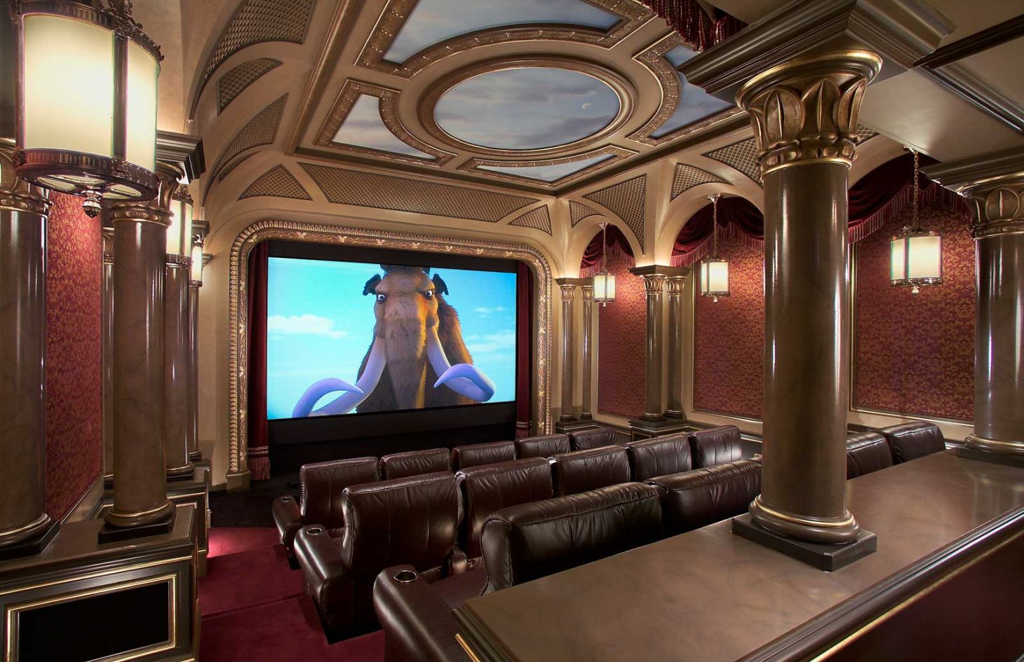 Traditional theater room with leather recliners in two rows, surrounded by ornate columns, red damask walls, and an overhead painted ceiling.